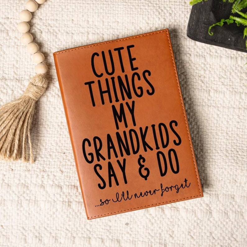 May include: A brown leather journal with the text "Cute Things My Grandkids Say & Do...so I'll never forget" in black lettering.