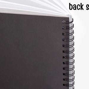 May include: The back side of a black spiral bound notebook. The notebook has a black cover and a silver spiral binding.