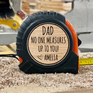 May include: A black and orange tape measure with a wooden plaque that reads "Dad No One Measures Up To You! Amelia".
