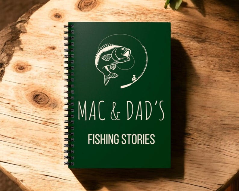 May include: A dark green spiral bound notebook with a white illustration of a fish jumping out of the water with a fishing rod. The text "MAC & DAD'S FISHING STORIES" is printed in white on the cover.