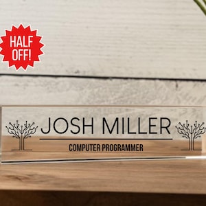 May include: A clear acrylic desk nameplate with a black design of stylized trees with circuit board patterns. The nameplate reads "Josh Miller, Computer Programmer".