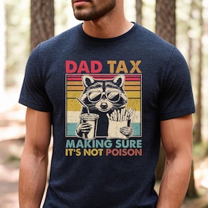 K&ouml;nnte beinhalten: Marineblaues T-Shirt mit einem Waschb&auml;ren mit Sonnenbrille, der ein Getr&auml;nk und Pommes h&auml;lt. Das Shirt hat den Text "DAD TAX" &uuml;ber dem Waschb&auml;ren und "MAKING SURE IT'S NOT POISON" darunter.