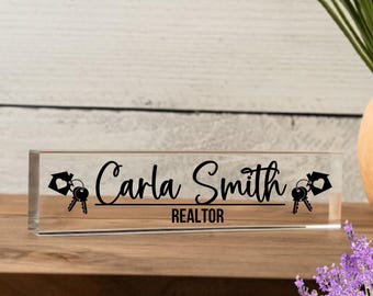 Może przedstawiać: Przezroczysta akrylowa tabliczka na biurko z czarnym tekstem "Carla Smith REALTOR" i wzorem klucza do domu po obu stronach.