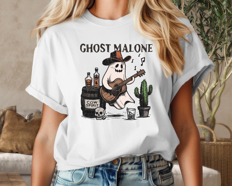May include: White t-shirt with a graphic of a ghost wearing a cowboy hat and playing a guitar. The text "Ghost Malone" is printed above the ghost. The ghost is holding a bottle of "Cow Spirit" liquor.