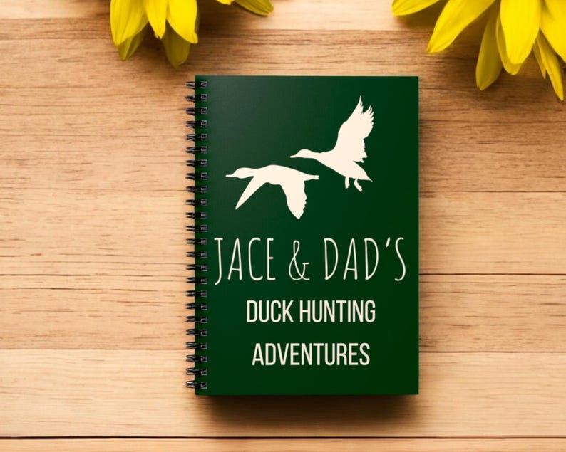 May include: A green spiral bound notebook with white silhouettes of ducks flying. The notebook has the text "Jace & Dad's Duck Hunting Adventures" printed on the front.