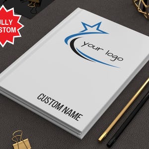 May include: White notebook with a blue and black star design and the text "your logo". The notebook also has the text "CUSTOM NAME" printed on the cover.