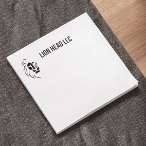 以下が含まれることがあります： 上部に黒で「LION HEAD LLC」と印刷された白いメモ帳。左上の隅にライオンの頭の白黒のイラストがあります。