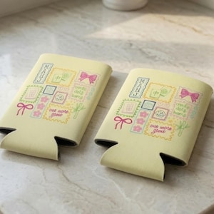 Puede incluir: Dos aislantes para bebidas de color amarillo p&aacute;lido con un estampado gr&aacute;fico colorido de fichas de Mahjong, lazos rosas, flores de cerezo y tallos de bamb&uacute; verdes. El texto "MAHJ" y "one more game" aparece entre los iconos.