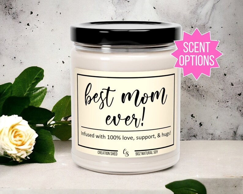 K&ouml;nnte beinhalten: Eine wei&szlig;e 255g-Kerze aus nat&uuml;rlichem Sojawachs in einem Glas mit schwarzem Deckel. Auf dem Etikett steht "best mom ever!" mit dem Text "Infused with 100% love, support, & hugs!" und "SCENT OPTIONS" in einem rosa Stern.
