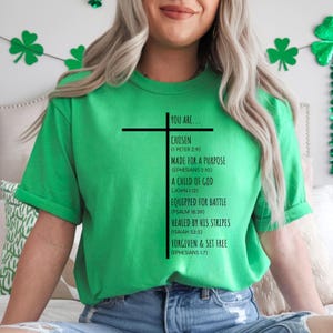 May include: Green t-shirt with a black cross and the text "YOU ARE... CHOSEN (1 PETER 2:9) MADE FOR A PURPOSE (EPHESIANS 2:10) A CHILD OF GOD (JOHN 1:12) EQUIPPED FOR BATTLE (PSALM 18:39) HEALED BY HIS STRIPES (ISAIAH 53:5) FORGIVEN & SET FREE (EPHESIANS 1:7)"