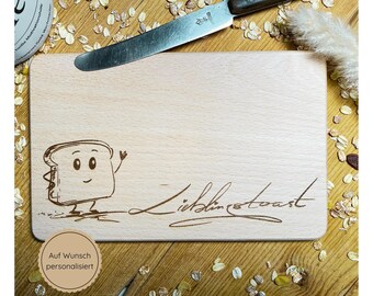 May include: A wooden cutting board with a cartoon toast design and the text "Lieblingstoast" engraved on it. The board is surrounded by oats and a knife.