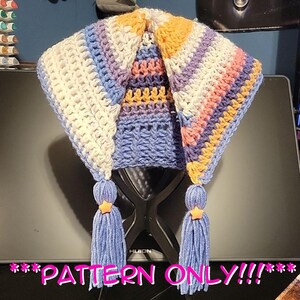 May include: A colourful, handmade crochet hat. The hat is made with white, blue, purple, and orange yarn. It has long, pointed flaps and tassels with star-shaped accents. The text "PATTERN ONLY!!!" is displayed at the bottom.