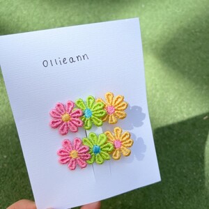 May include: Two sets of colorful flower hair clips. Each set has three flowers in pink, yellow, and green.