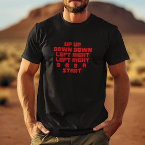 Puede incluir: Camiseta negra con texto rojo que dice "Up Up Down Down Left Right Left Right B A B A Start".