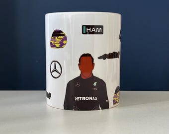 May include: White ceramic mug featuring a stylized illustration of a Formula 1 driver. The mug includes the driver's silhouette, helmet, car, and the word "HAM". The mug has a black and yellow design.