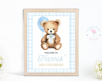 May include: A blue and white gingham patterned printable sign with a brown teddy bear holding a blue balloon. The sign says "Welcome to Harris' Bear-y First Birthday".