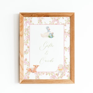 May include: A framed sign with a floral border and a white background. The sign says "Gifts & Cards" in gold lettering. There are illustrations of a duck, a lamb, and a basket of eggs.
