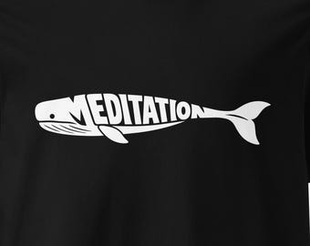 Könnte beinhalten: Ein schwarzes T-Shirt mit kurzen Ärmeln und einer weißen Wal-Grafik auf der Brust. Der Körper des Wals wird durch das Wort MEDITATION in fetten Großbuchstaben gebildet. Das Design ist mittig auf der Vorderseite des Kleidungsstücks platziert.