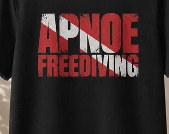Puede incluir: Una camiseta negra de manga corta con un estampado gráfico en el pecho. El diseño muestra la palabra APNOE sobre la palabra FREEDIVING en una fuente roja desgastada, superpuesta a una franja diagonal blanca que recuerda a una bandera de buceo.