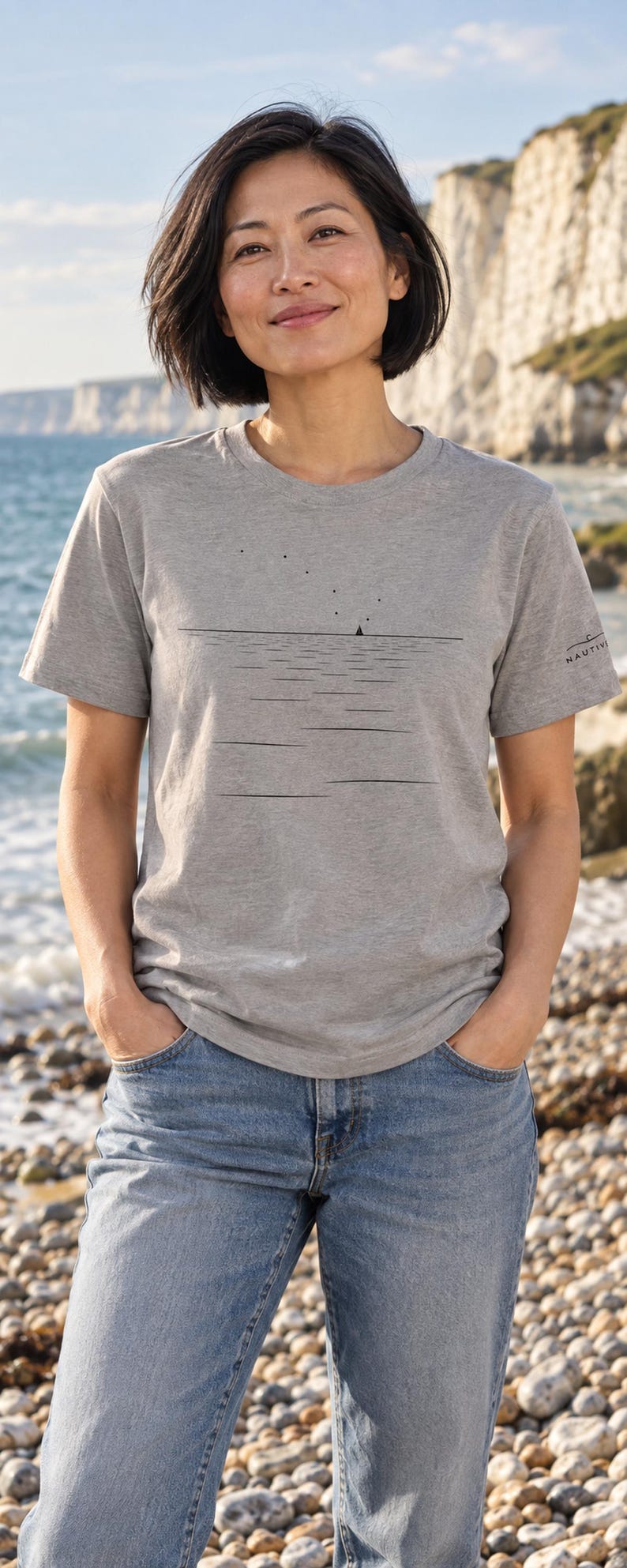 Peut inclure: Un t-shirt gris chin&eacute; &agrave; manches courtes avec un motif noir minimaliste repr&eacute;sentant une ligne d'horizon, un petit voilier et des points dispers&eacute;s au-dessus. Le mot NAUTIVE est imprim&eacute; en petites lettres noires sur la manche gauche.