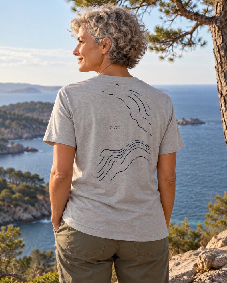K&ouml;nnte beinhalten: Ein hellgraues Kurzarm-T-Shirt mit einem dunkelblauen Grafikdruck topografischer Linien auf der R&uuml;ckseite. Der Druck enth&auml;lt den Text -1200 m ATLANTIC. Das T-Shirt hat einen Rundhalsausschnitt und eine Standardpassform aus meliertem Stoff.