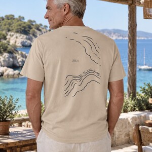 K&ouml;nnte beinhalten: Ein beiges Kurzarm-T-Shirt mit einer dunkelblauen Linien-Grafik auf der R&uuml;ckseite. Das Design zeigt abstrakte topografische Wellenmuster und enth&auml;lt den aufgedruckten Text -1200 m ATLANTIC. Das T-Shirt hat einen Rundhalsausschnitt und eine Standardpassform.
