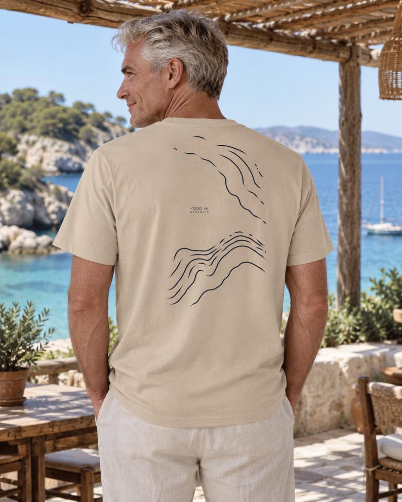 K&ouml;nnte beinhalten: Ein beiges Kurzarm-T-Shirt mit einer dunkelblauen Linien-Grafik auf der R&uuml;ckseite. Das Design zeigt abstrakte topografische Wellenmuster und enth&auml;lt den aufgedruckten Text -1200 m ATLANTIC. Das T-Shirt hat einen Rundhalsausschnitt und eine Standardpassform.