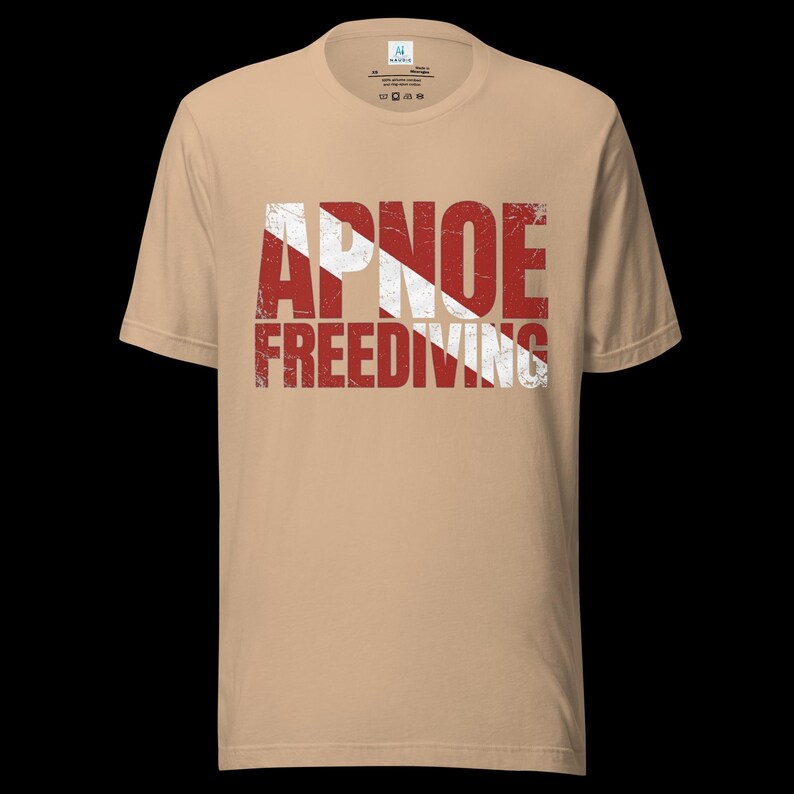 Puede incluir: Una camiseta de manga corta color canela con un estampado gr&aacute;fico desgastado en rojo y blanco en el pecho. El dise&ntilde;o muestra el texto APNOE y FREEDIVING superpuesto sobre una franja blanca diagonal, imitando el dise&ntilde;o de una bandera de buceo.