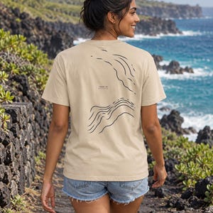 K&ouml;nnte beinhalten: Ein beiges Kurzarm-T-Shirt mit einer schwarzen Linien-Grafik auf der R&uuml;ckseite. Das Design zeigt abstrakte topografische Wellenmuster und enth&auml;lt den aufgedruckten Text -1200 m ATLANTIC. Das T-Shirt hat einen Rundhalsausschnitt und eine Standardpassform.