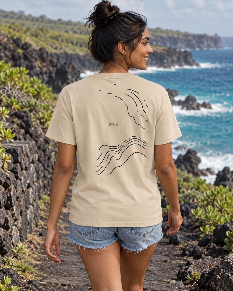 K&ouml;nnte beinhalten: Ein beiges Kurzarm-T-Shirt mit einer schwarzen Linien-Grafik auf der R&uuml;ckseite. Das Design zeigt abstrakte topografische Wellenmuster und enth&auml;lt den aufgedruckten Text -1200 m ATLANTIC. Das T-Shirt hat einen Rundhalsausschnitt und eine Standardpassform.