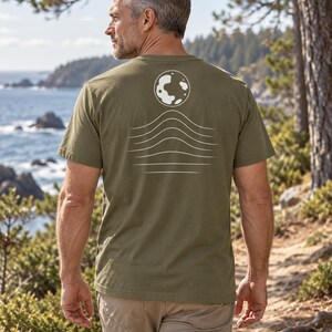 K&ouml;nnte beinhalten: Ein olivgr&uuml;nes Kurzarm-T-Shirt mit einer wei&szlig;en Grafik auf der R&uuml;ckseite. Das Design besteht aus einer kreisf&ouml;rmigen Mondform &uuml;ber einer Reihe von f&uuml;nf horizontalen, wellenf&ouml;rmigen Linien, die nach unten hin allm&auml;hlich flacher werden.