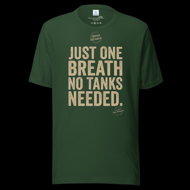 May include: A dark green short-sleeve t-shirt featuring the beige text "JUST ONE BREATH NO TANKS NEEDED." centered on the chest. Above the text is a circular logo with the words "Apnea Division." and below is a small circular emblem.