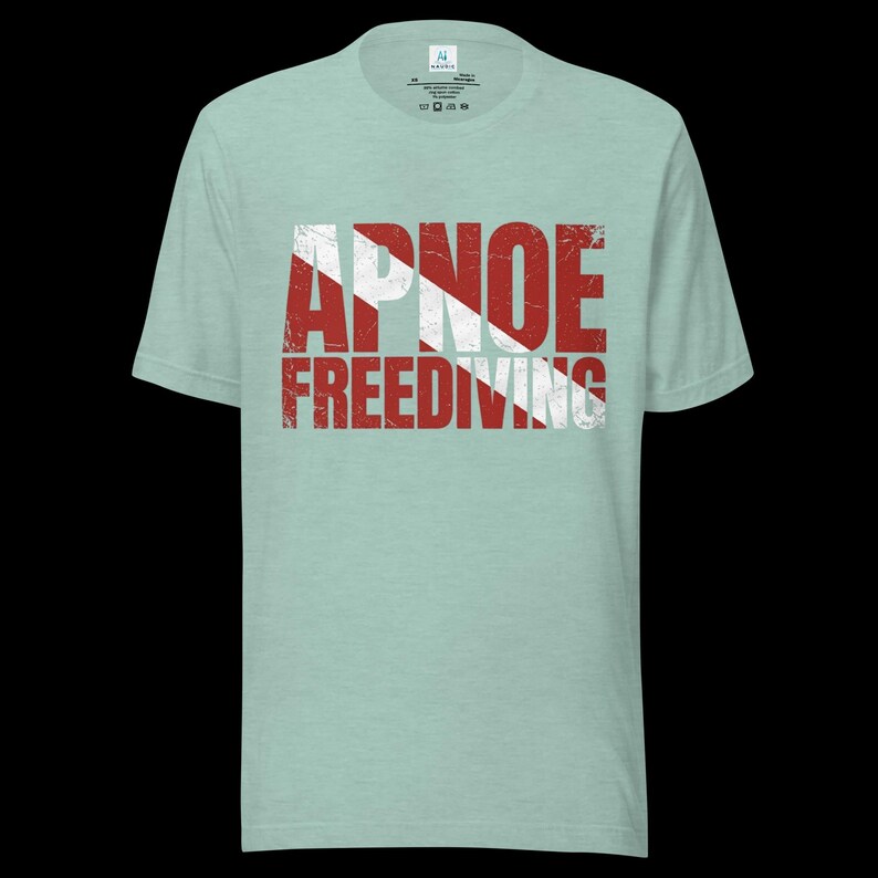 Puede incluir: Una camiseta de manga corta de color verde claro con un estampado gr&aacute;fico desgastado en rojo y blanco en el pecho. El gr&aacute;fico muestra el texto APNOE FREEDIVING superpuesto a un patr&oacute;n de rayas diagonales rojas y blancas que recuerda a una bandera de buceo.