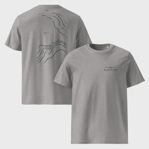K&ouml;nnte beinhalten: Ein graumeliertes Kurzarm-T-Shirt mit einer schwarzen Linien-Grafik auf der linken Brust und dem Schriftzug NAUTIVE darunter. Auf der R&uuml;ckseite des T-Shirts befindet sich ein gro&szlig;es schwarzes Liniendesign mit abstrakten Wellenmustern.