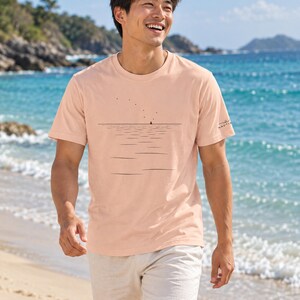 Peut inclure: Un t-shirt &agrave; manches courtes de couleur p&ecirc;che avec un graphisme au trait noir repr&eacute;sentant une ligne d'horizon, un petit voilier et une s&eacute;rie de points &eacute;voquant des oiseaux. La manche porte un petit logo noir avec le texte NAUTICA.