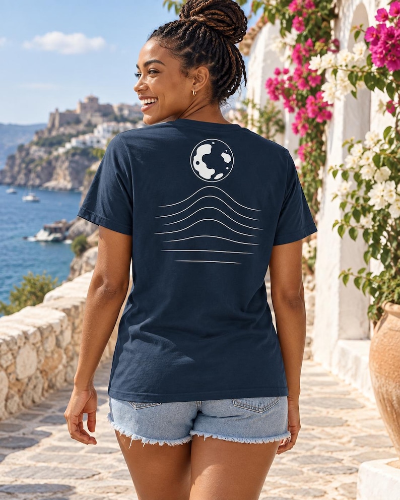 K&ouml;nnte beinhalten: Ein dunkelblaues T-Shirt mit kurzen &Auml;rmeln und einer wei&szlig;en Grafik auf der R&uuml;ckseite. Das Design besteht aus einer kreisf&ouml;rmigen Mondform &uuml;ber einer Reihe von f&uuml;nf horizontalen, wellenf&ouml;rmigen Linien, die nach unten hin k&uuml;rzer werden.
