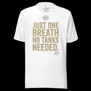 May include: A white short-sleeve t-shirt featuring the text "JUST ONE BREATH NO TANKS NEEDED." in a distressed tan font. Above the text is a circular "Apnea Division" logo, and below the text is a smaller circular "Est. 2019 Pure Freedom" logo.