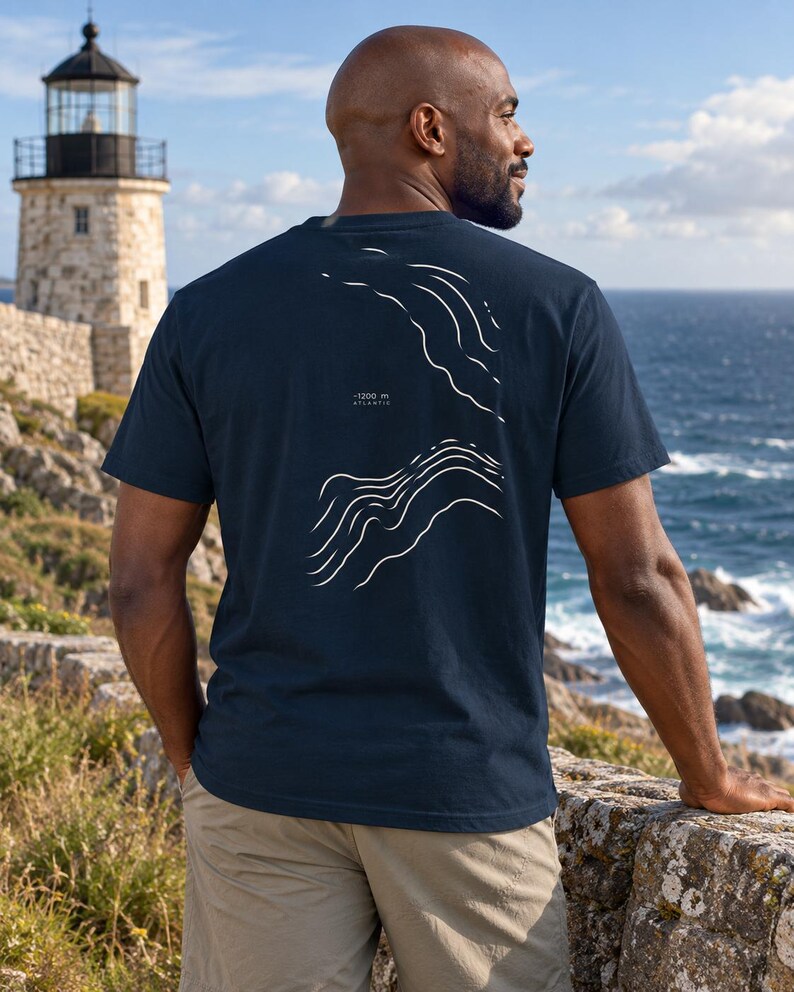 K&ouml;nnte beinhalten: Ein dunkelblaues Kurzarm-T-Shirt mit einer wei&szlig;en Strichgrafik auf der R&uuml;ckseite. Das Design zeigt abstrakte topografische Wellenmuster und enth&auml;lt den aufgedruckten Text -1200 m ATLANTIC zwischen den beiden Wellenillustrationen.
