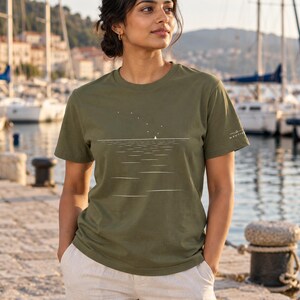 Peut inclure: Un t-shirt vert olive &agrave; manches courtes avec une impression graphique blanche repr&eacute;sentant un petit voilier sur l'eau sous un ciel &eacute;toil&eacute;. Le motif comprend une ligne d'horizon horizontale et le mot NAUTIV imprim&eacute; sur la manche gauche en blanc.