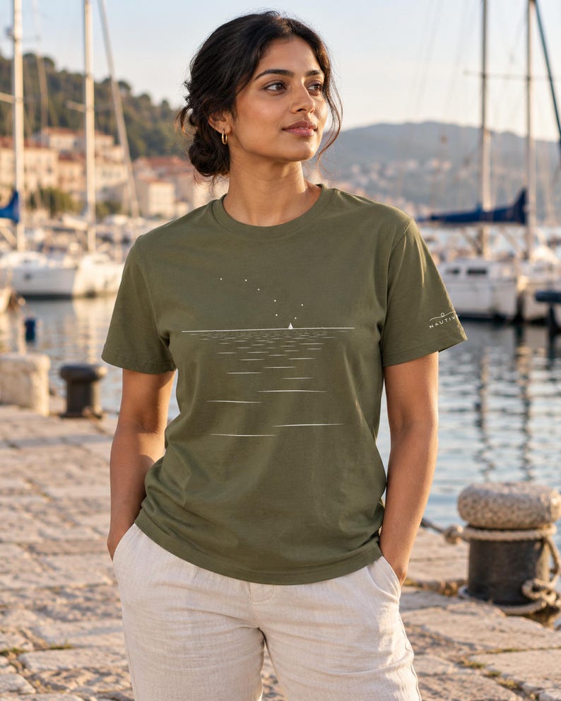 Peut inclure: Un t-shirt vert olive &agrave; manches courtes avec une impression graphique blanche repr&eacute;sentant un petit voilier sur l'eau sous un ciel &eacute;toil&eacute;. Le motif comprend une ligne d'horizon horizontale et le mot NAUTIV imprim&eacute; sur la manche gauche en blanc.