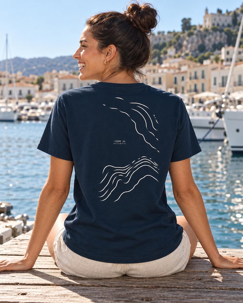 K&ouml;nnte beinhalten: Ein dunkelblaues Kurzarm-T-Shirt mit einer wei&szlig;en Linien-Grafik auf der R&uuml;ckseite. Das Design zeigt abstrakte topografische Wellenmuster mit dem Text -1200 m ATLANTIC, der mittig zwischen den beiden Wellenabschnitten aufgedruckt ist.