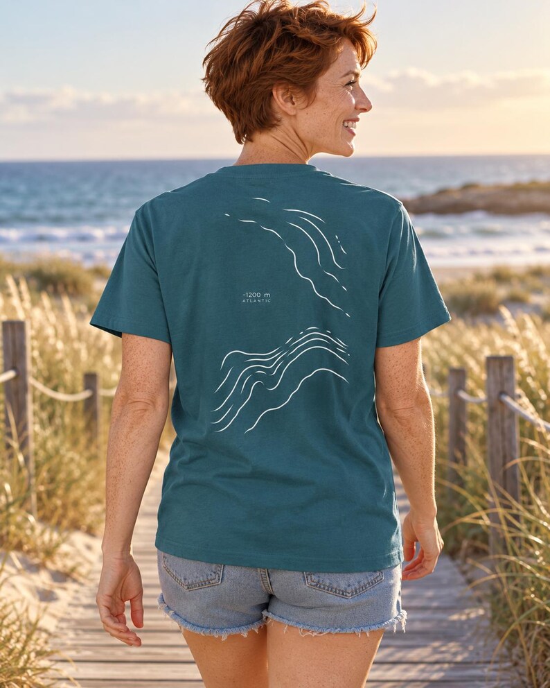 K&ouml;nnte beinhalten: Ein blaugr&uuml;nes Kurzarm-T-Shirt mit einer wei&szlig;en Linien-Grafik auf der R&uuml;ckseite. Das Design zeigt abstrakte Wellenmuster und enth&auml;lt den Text -1200 m ATLANTIC, der in Wei&szlig; zwischen den beiden Wellenillustrationen auf dem R&uuml;cken gedruckt ist.