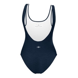 Könnte beinhalten: Ein einteiliger Badeanzug aus dunkelblauem Stoff mit einer dezenten Wellenstruktur. Der Text lautet CURRENT COLLECTION INSPIRED BY THE OCEAN, 4 OCEAN INSPIRED COLORS, MIDNIGHT BLACK, MIDNIGHT NAVY, OCEAN GREEN, SAND und NAUTIVE.