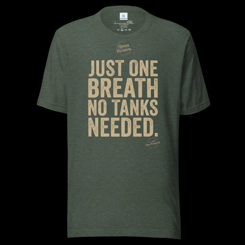 May include: A heathered olive green short-sleeve t-shirt featuring the beige text "JUST ONE BREATH NO TANKS NEEDED." and the "Apnea Division" logo printed on the chest. The shirt has a crew neckline and a standard fit for casual wear.