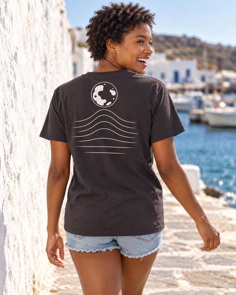 K&ouml;nnte beinhalten: Ein anthrazitfarbenes Kurzarm-T-Shirt mit einer wei&szlig;en Grafik auf der R&uuml;ckseite. Das Design besteht aus einer kreisf&ouml;rmigen Mondform &uuml;ber einer Reihe von f&uuml;nf horizontalen, wellenf&ouml;rmigen Linien, die zum unteren Rand des Shirts hin flacher werden.