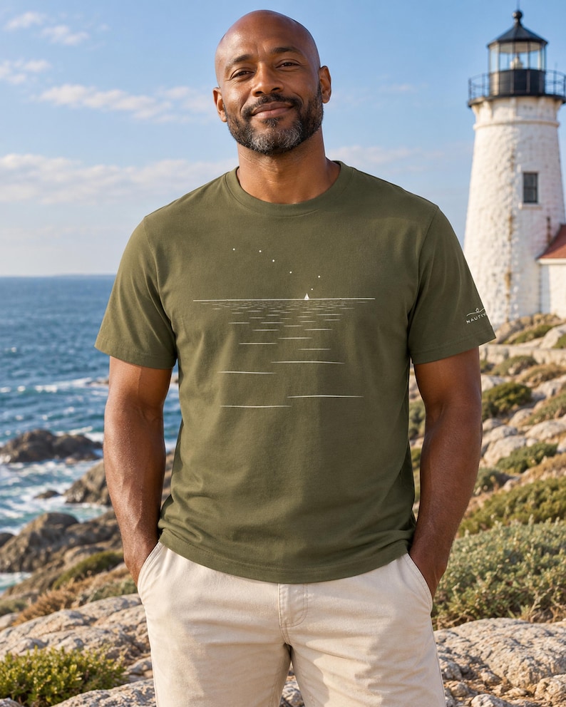 Peut inclure: Un t-shirt &agrave; col rond et manches courtes vert olive avec un motif graphique blanc repr&eacute;sentant un petit voilier &agrave; l'horizon sous un ciel &eacute;toil&eacute;, incluant un petit logo blanc sur la manche gauche et un ourlet droit &agrave; la taille.