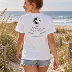 K&ouml;nnte beinhalten: Ein wei&szlig;es kurz&auml;rmeliges T-Shirt mit einer schwarzen Grafik auf der R&uuml;ckseite. Das Design besteht aus einer kreisf&ouml;rmigen Mondform &uuml;ber einer Reihe von f&uuml;nf horizontalen Wellenlinien, die sich zur Mitte hin kr&uuml;mmen und eine minimalistische Landschaft bilden.