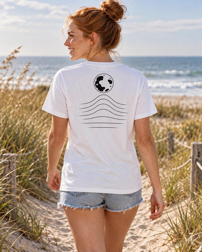 K&ouml;nnte beinhalten: Ein wei&szlig;es kurz&auml;rmeliges T-Shirt mit einer schwarzen Grafik auf der R&uuml;ckseite. Das Design besteht aus einer kreisf&ouml;rmigen Mondform &uuml;ber einer Reihe von f&uuml;nf horizontalen Wellenlinien, die sich zur Mitte hin kr&uuml;mmen und eine minimalistische Landschaft bilden.