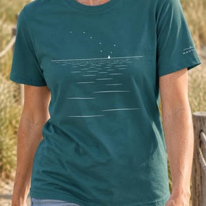 Peut inclure: Un t-shirt &agrave; col rond et manches courtes de couleur sarcelle, orn&eacute; d'un motif graphique blanc repr&eacute;sentant un voilier sur l'eau sous un ciel &eacute;toil&eacute;. Le v&ecirc;tement pr&eacute;sente un petit logo blanc sur la manche gauche et une coupe droite classique.