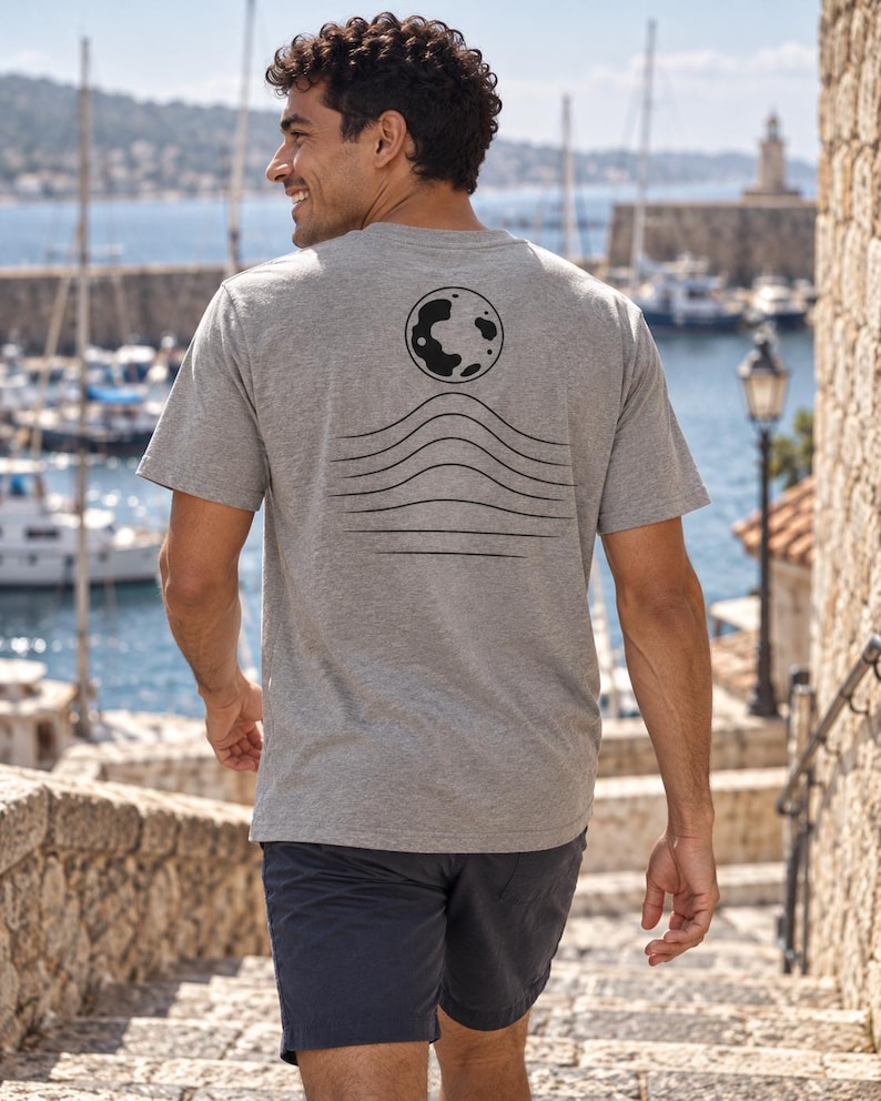 K&ouml;nnte beinhalten: Ein kurz&auml;rmeliges T-Shirt in Grau meliert mit einer schwarzen Grafik auf der R&uuml;ckseite. Das Design besteht aus einer kreisf&ouml;rmigen Mondform &uuml;ber einer Reihe von sechs horizontalen, wellenf&ouml;rmigen Linien, die nach unten hin breiter werden.